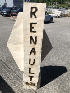Vue d'ensemble d'une sculpture monumentale du logo Renault en bois, exposée en extérieur.