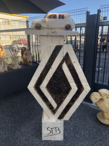 Gros plan sur la gravure verticale du mot "RENAULT" et le sigle "A2L" sur le totem en bois sculpté.