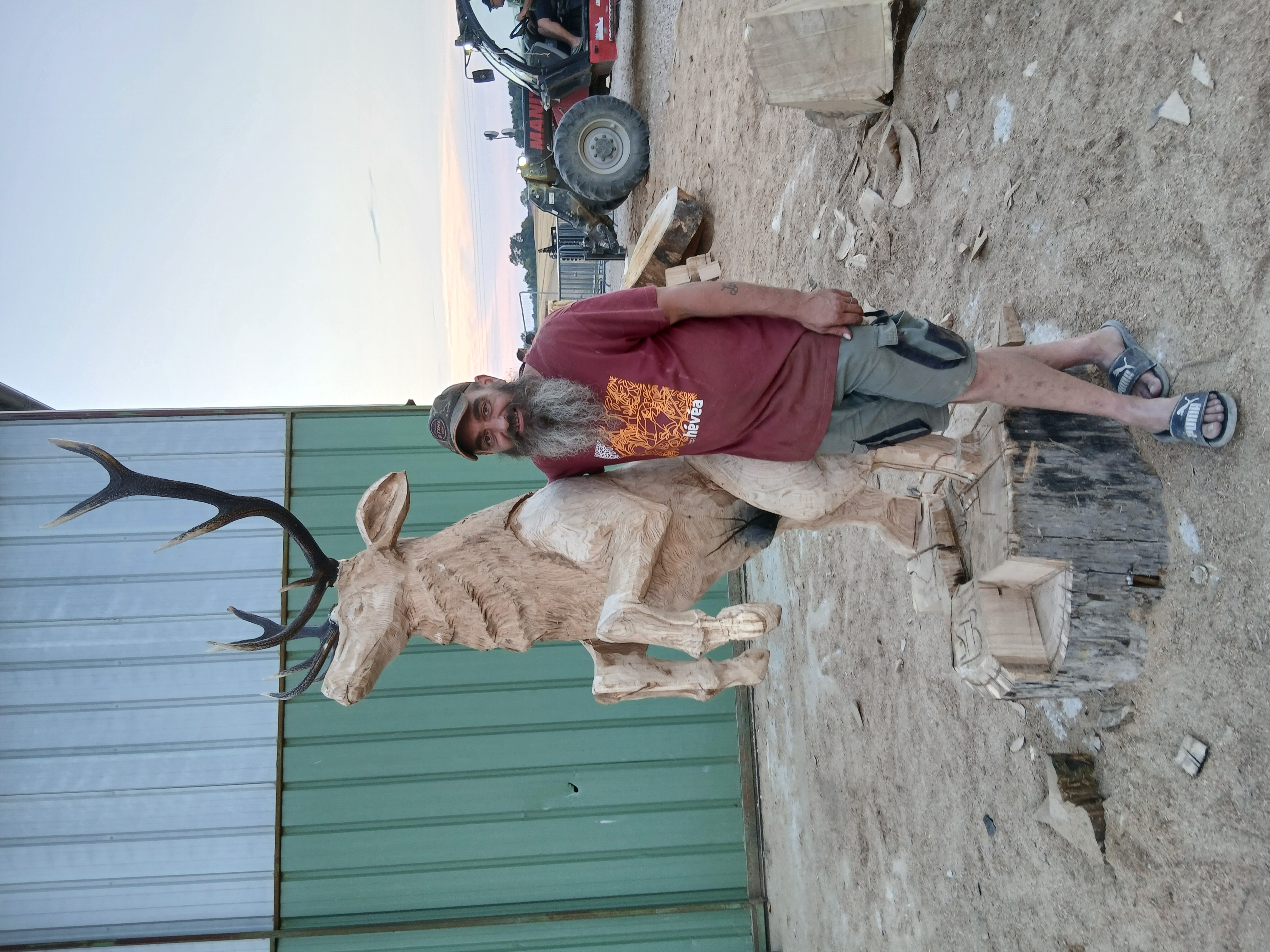 Le sculpteur Sébastien Steffen posant fièrement à côté de sa sculpture de cerf en bois fraîchement achevée.