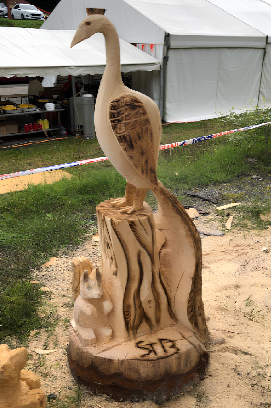 Sculpture sur bois d'un oiseau (pélican ou héron) au long cou, perché sur une souche sculptée, par Sébastien Steffen.
